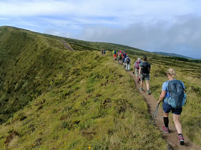 Wandergruppe auf einem Pfad entlang eines grünen Hügels.