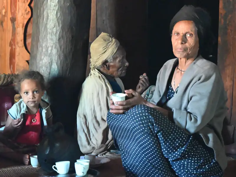 Drei Generationen einer Familie sitzen beisammen: Ein kleines Kind, eine ältere Frau und eine weitere ältere Person.