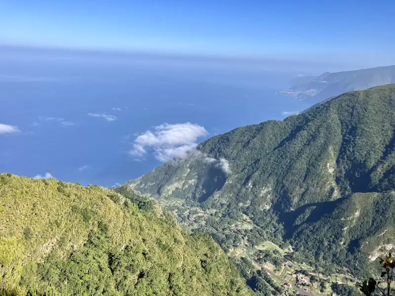 Blick von einem Berghang auf bewaldete Hänge, die zum Meer hin abfallen.