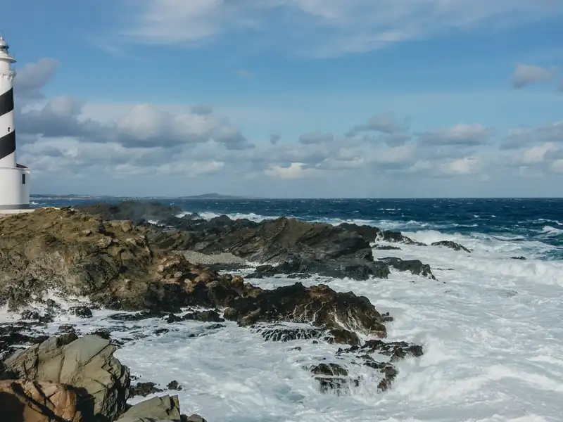 Schwarz-weißer Leuchtturm an felsiger Küste mit Wellengang.