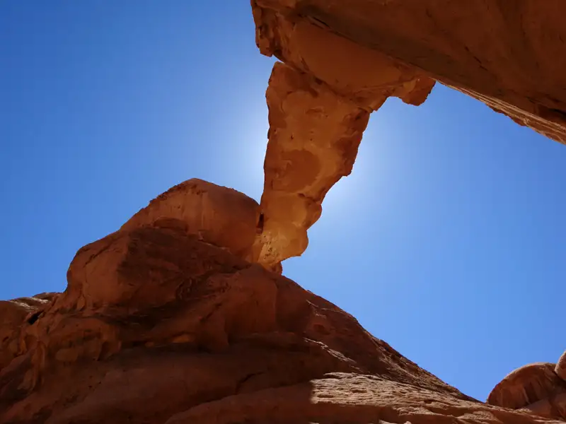 Natürliche Felsformation einer Brücke aus rotem Gestein vor blauem Himmel.