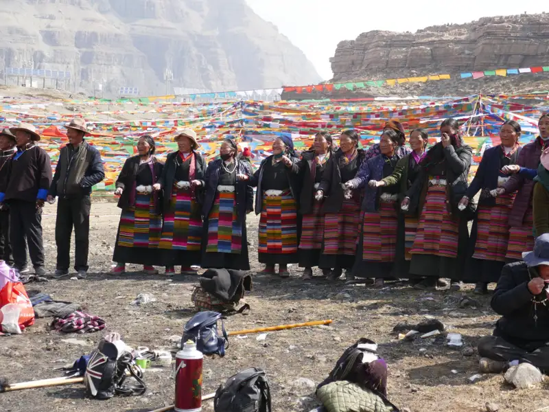 Einheimische in traditioneller Kleidung nehmen an einer Zeremonie vor einer Gebetsfahnenlandschaft teil.