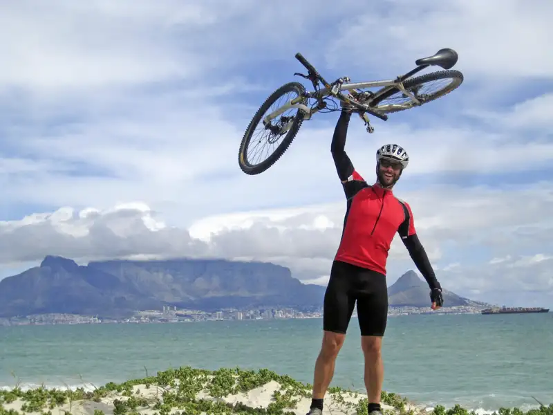 Erfolgreicher Abschluss einer Radtour: Radfahrer mit erhobenem Fahrrad vor dem Tafelberg.