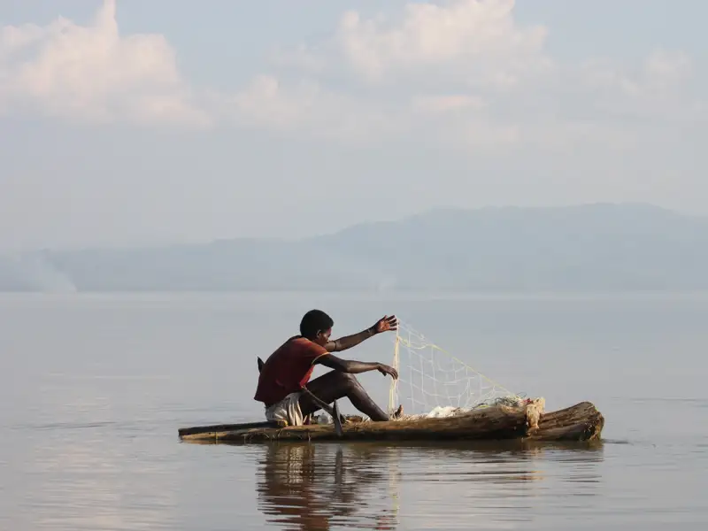 Fischer auf einem Einbaum beim Fischen mit Netz.