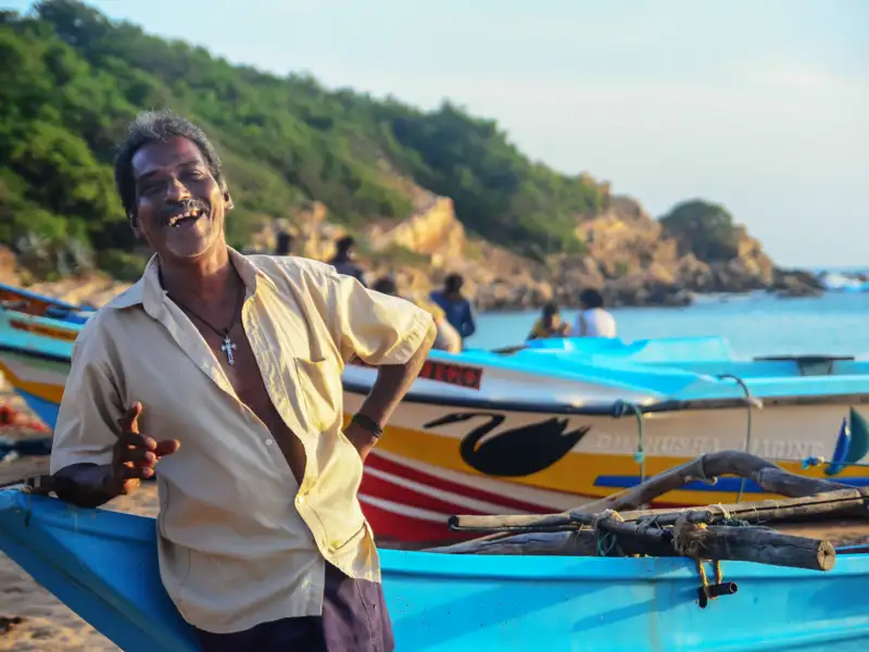 Ein Fischer an der Küste Sri Lankas neben seinem traditionellen Fischerboot.