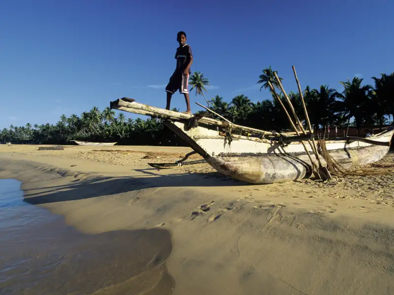 Traditionelles Fischerboot am Strand mit einem Jungen.