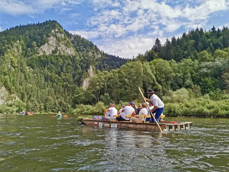 Touristen auf einer traditionellen Floßfahrt auf dem Fluss, umgeben von der natürlichen Schönheit der bewaldeten Hügel.