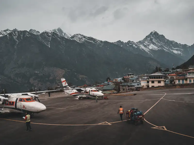 Flugzeuge auf einem Bergflughafen mit schneebedeckten Gipfeln im Hintergrund.