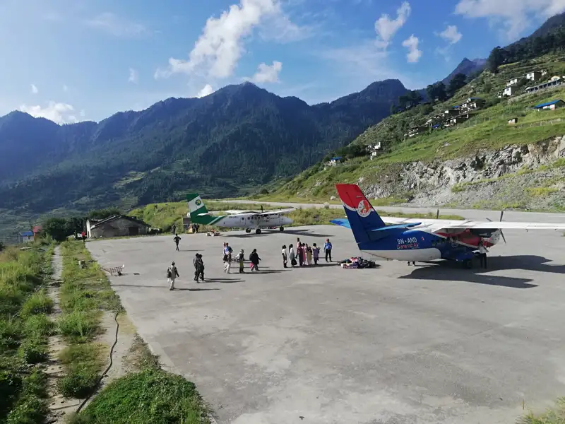 Zwei Flugzeuge auf einem Bergflughafen, umgeben von Passagieren und Gepäck.