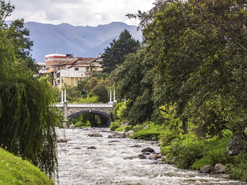 Fluss mit Brücke und Bergen im Hintergrund.