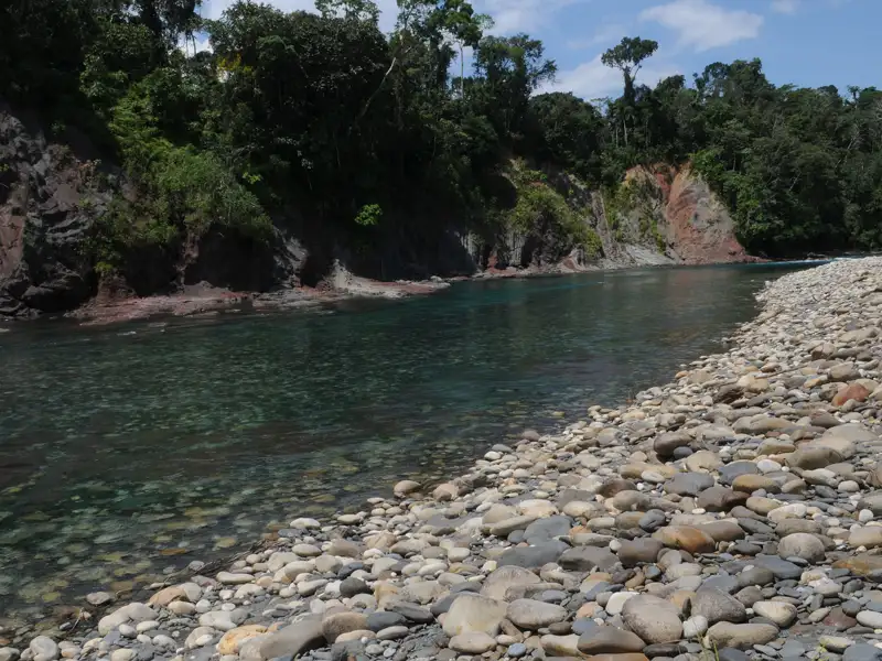 Klares Flusswasser, Kieselstrand und bewaldete Ufer.