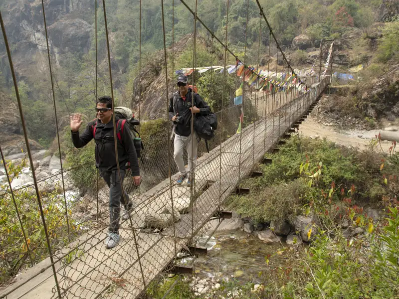 Wanderer überqueren eine Hängebrücke im Gebirge.