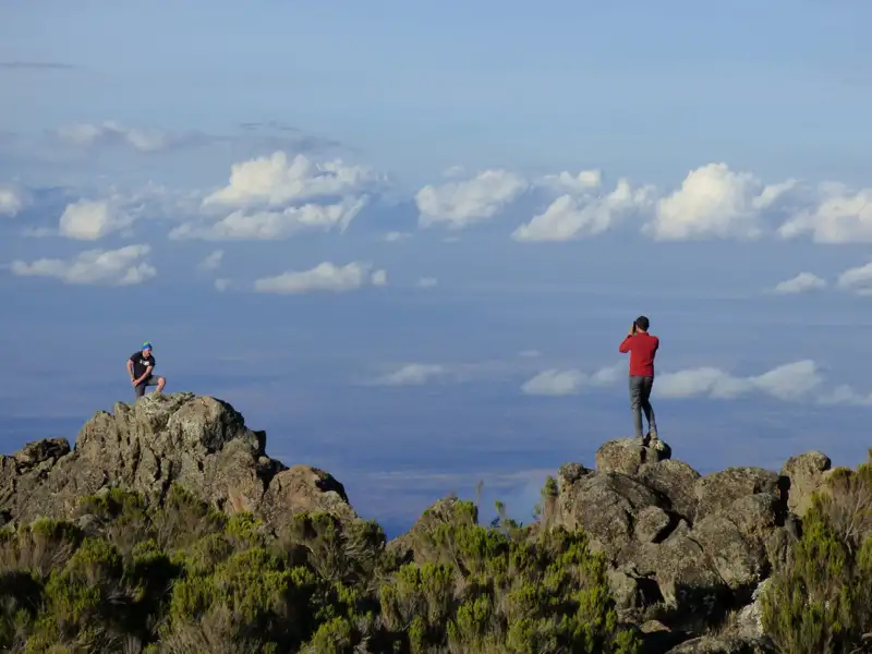 Zwei Personen stehen auf Felsvorsprüngen und betrachten die Landschaft. Einer fotografiert.