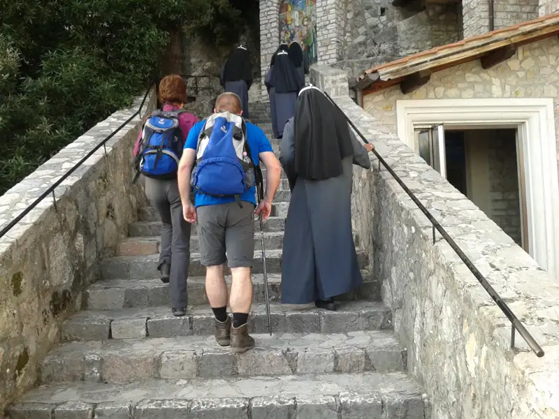 Wanderer und Nonnen besteigen eine Steintreppe, möglicherweise im Rahmen einer Pilgerreise oder eines Besuchs eines religiösen Ortes.