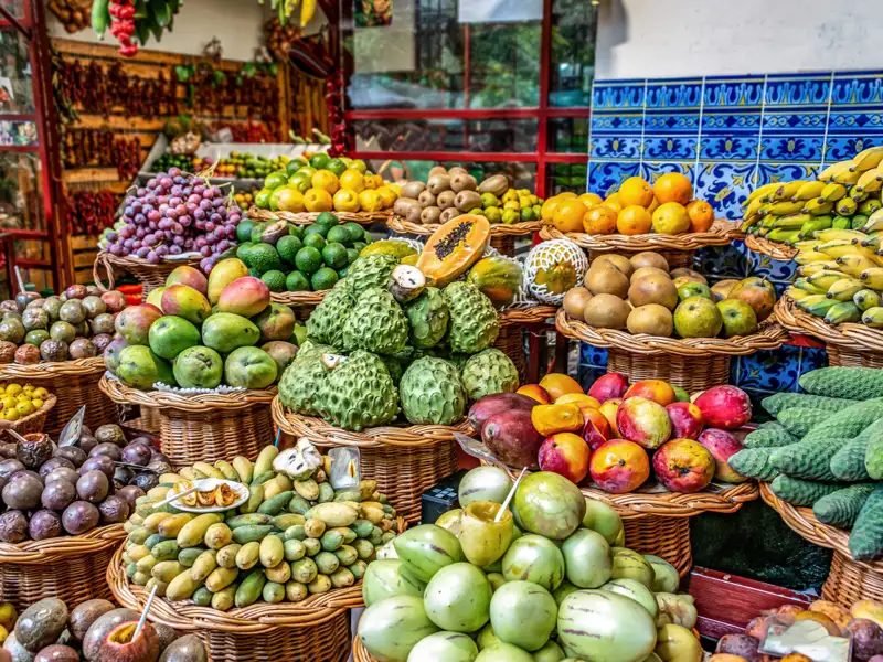 Verschiedene tropische Früchte wie Mangos, Passionsfrüchte, Bananen und Ananas, ausgestellt in Körben auf einem Marktstand.