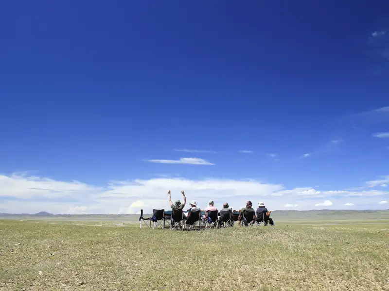 Reisende genießen eine Pause auf ihrer Reise und sitzen auf Campingstühlen in einer weiten Ebene.