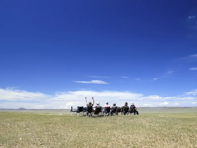 Reisende entspannen sich in Campingstühlen und genießen die Aussicht auf die weite Landschaft.