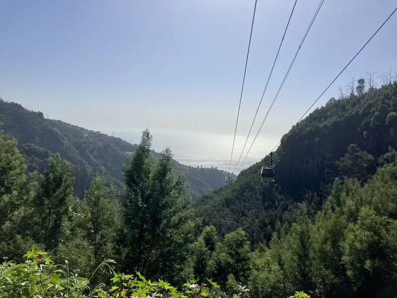 Seilbahn über einem bewaldeten Tal mit Blick auf das Meer.