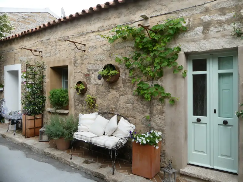 Eingangsbereich eines Steinhaus mit mintgrüner Tür und Bepflanzung.