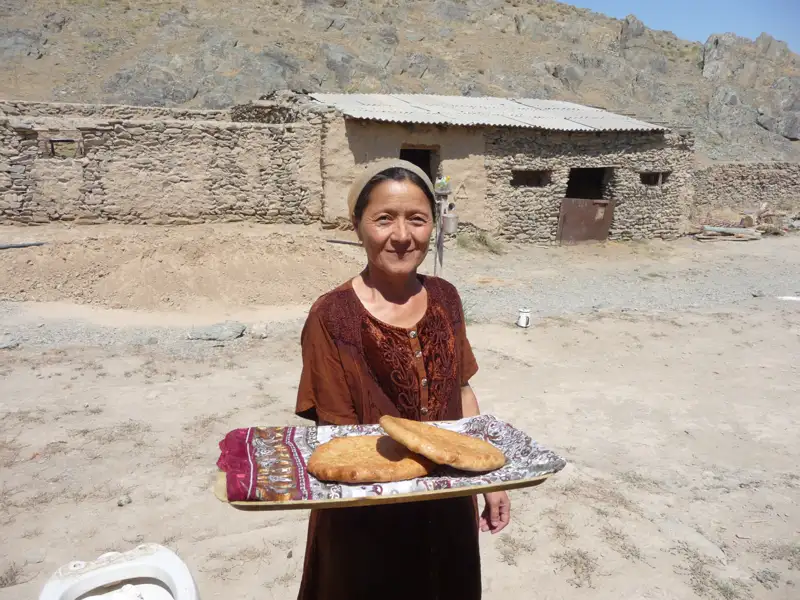 Frau mit traditionellem Fladenbrot vor einem Haus.