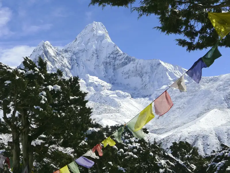Bunte Gebetsfahnen im Vordergrund mit Blick auf einen schneebedeckten Berg im Himalaya.