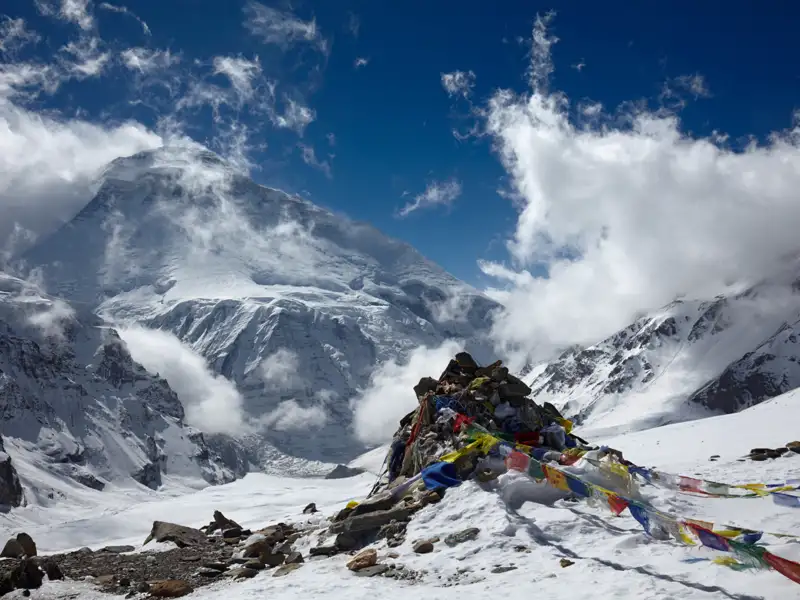 Gebetsfahnen im Schnee vor einem imposanten Bergmassiv im Himalaya.