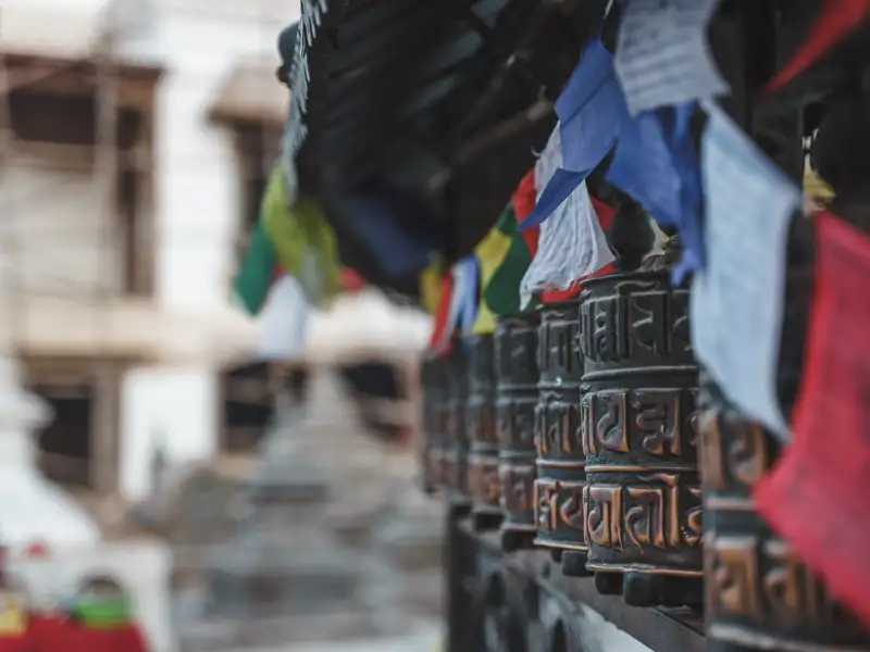 Gebetsmühlen mit tibetischen Mantras und flatternde Gebetsfahnen an einem Tempel.