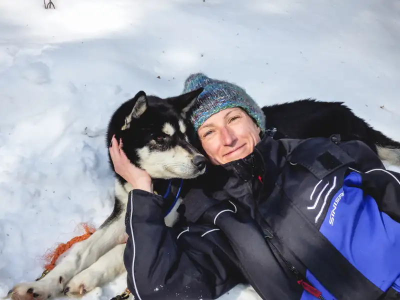 Person kuschelt mit Husky im Schnee.