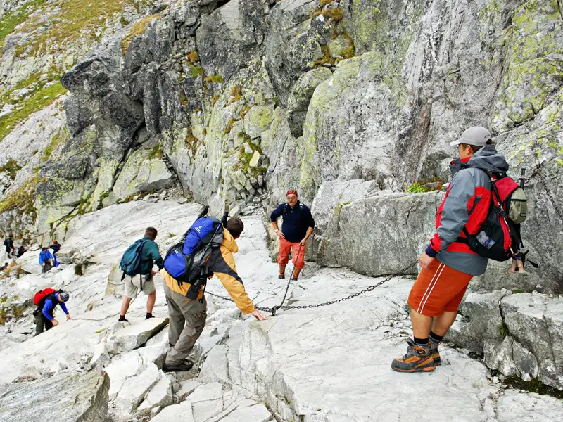 Wanderer nutzen Ketten zur Unterstützung beim Aufstieg eines anspruchsvollen Bergpfades.