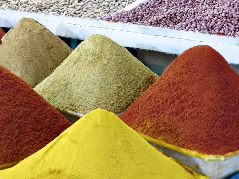 Verschiedene Gewürze, darunter rot, gelb und grün, pyramidenförmig auf einem Marktstand angeordnet.