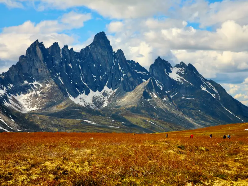 Wandergruppe in einer bergigen Landschaft mit herbstlicher Vegetation.