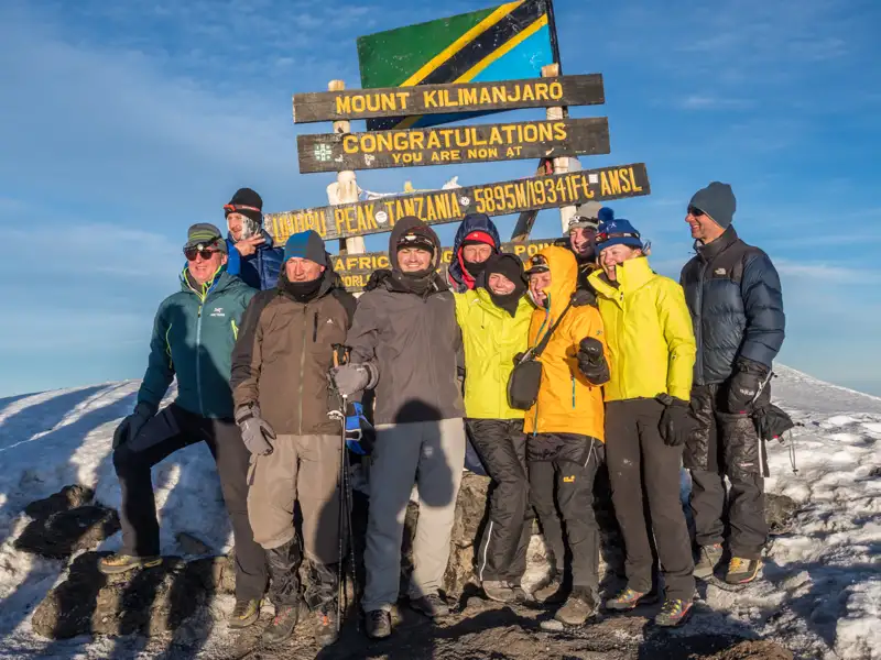 Wandergruppe feiert die erfolgreiche Besteigung des Uhuru Peak, dem höchsten Punkt des Kilimandscharo in Tansania.