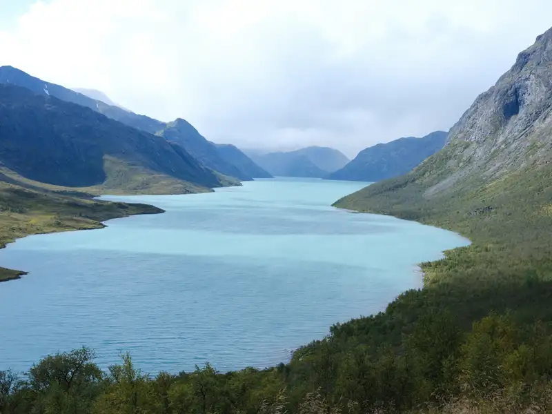 Panoramablick auf einen türkisfarbenen See inmitten einer Berglandschaft.