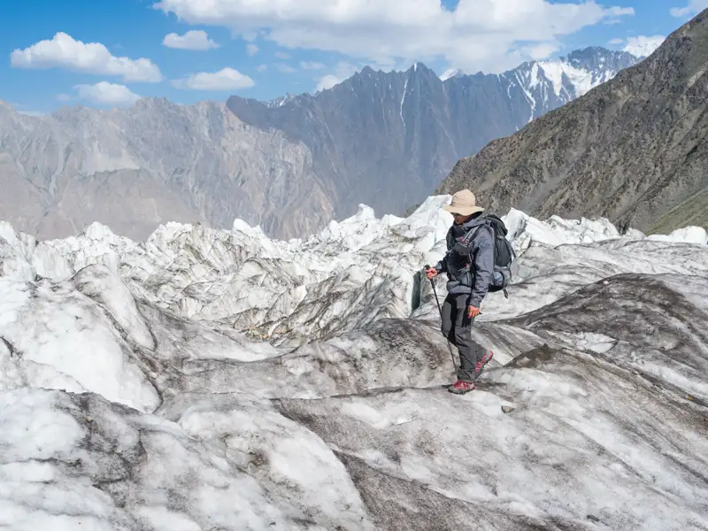 Wanderer mit Rucksack und Wanderstöcken überquert einen Gletscher vor der Kulisse schneebedeckter Berge.