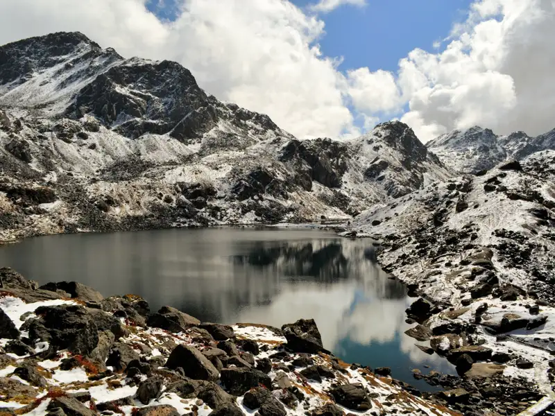 Bergsee mit schneebedeckten Gipfeln im Hintergrund.