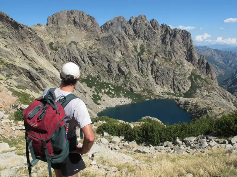 Wanderer mit Blick auf einen Bergsee inmitten einer felsigen Berglandschaft.
