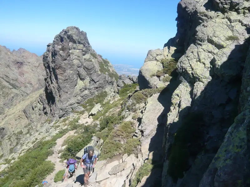 Wanderer auf einem Bergpfad mit felsigen Gipfeln im Hintergrund.