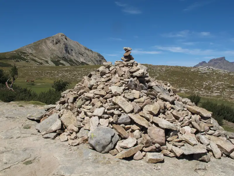 Ein Steinhaufen, der möglicherweise als Wegmarkierung dient, in einer Berglandschaft.