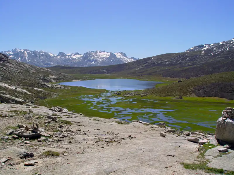 Panoramablick auf einen Bergsee mit schneebedeckten Gipfeln im Hintergrund.