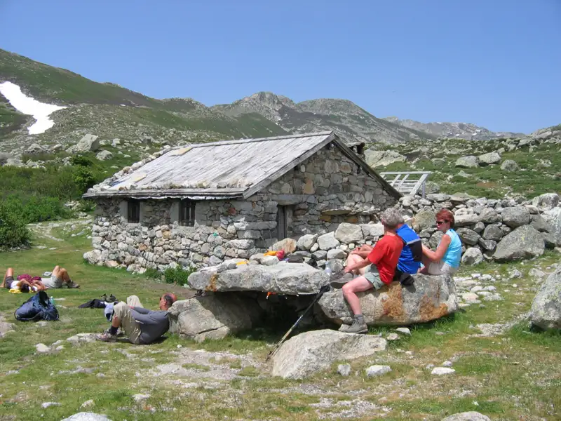 Rast während einer Wanderung: Wanderer pausieren vor einer Berghütte in den Bergen.
