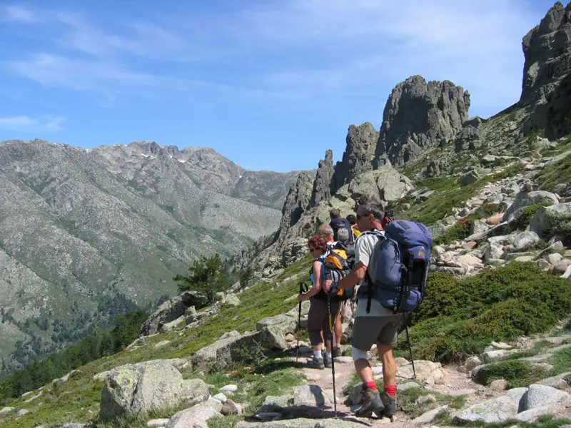 Wandergruppe auf einem Bergpfad mit felsigen Gipfeln im Hintergrund.