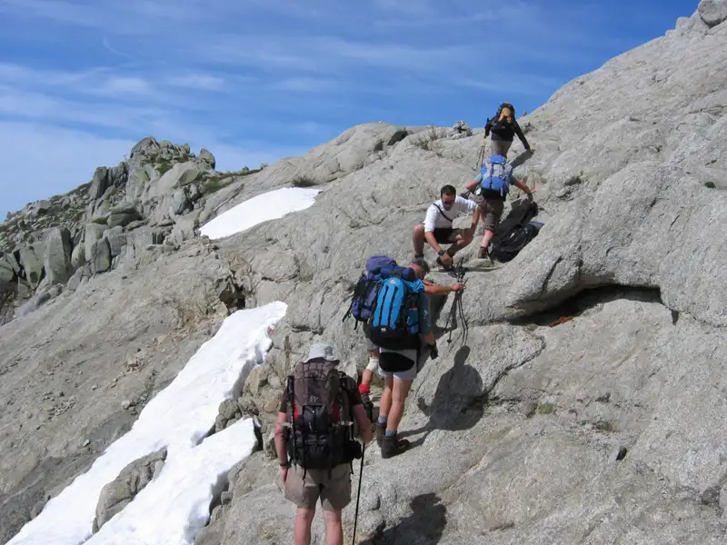 Wanderer auf einem anspruchsvollen Bergpfad mit Schneeresten.