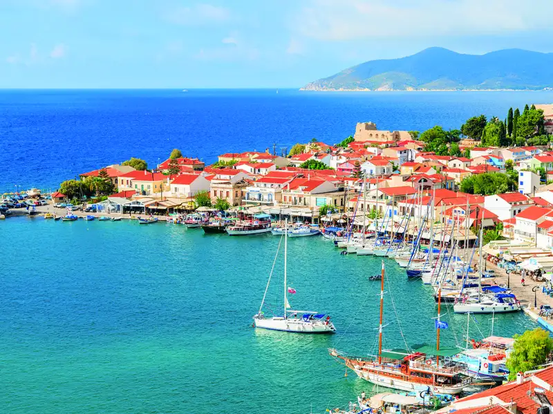 Hafenstadt mit traditionellen roten Dächern und Segelbooten im türkisblauen Wasser.