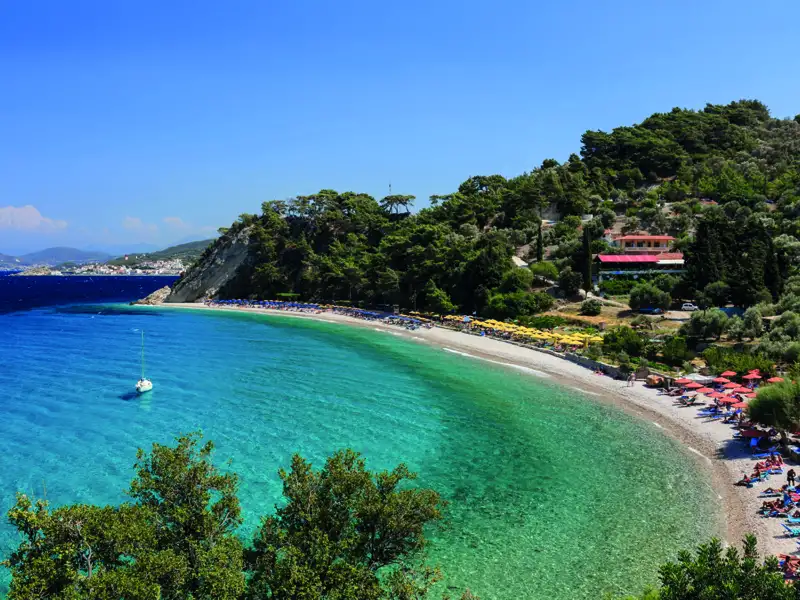 Türkisblaues Wasser, Sandstrand und bewaldete Küste einer Bucht.
