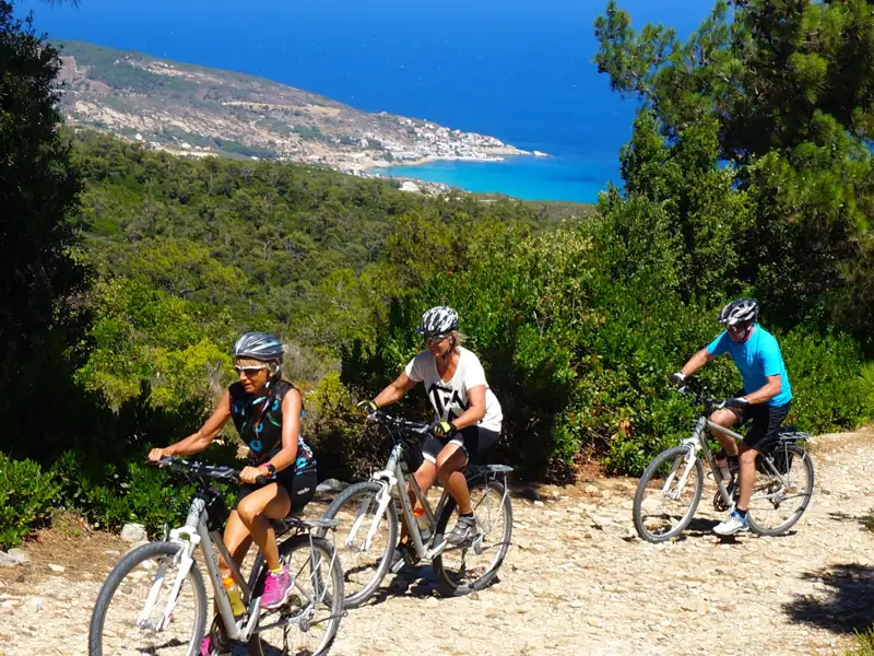 Drei Radfahrer genießen eine Radtour auf einem Küstenweg mit Blick auf das Meer und die Hügel.