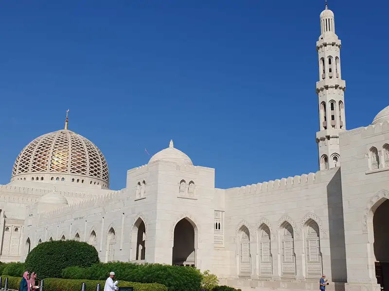 Sultan-Qabus-Moschee mit goldener Kuppel und Minarett unter blauem Himmel.