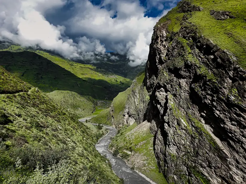 Blick auf einen Fluss, der sich durch ein Tal im Gebirge schlängelt. Steile Felswände und grüne Hänge prägen die Landschaft.