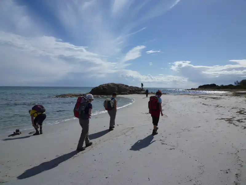 Wanderer mit Rucksäcken auf einer Strandwanderung.