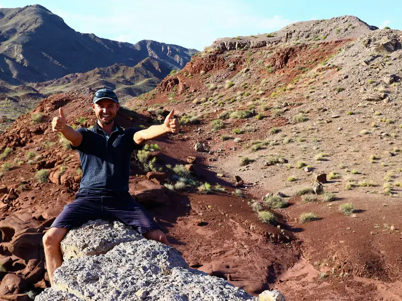 Reisender gibt Daumen hoch in der roten Felslandschaft.