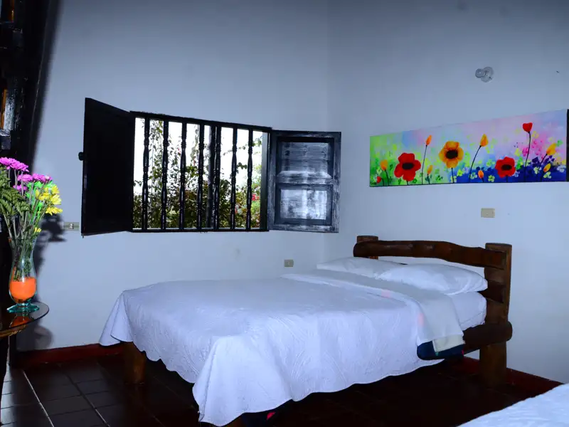 Doppelbett im Schlafzimmer mit Fenster und Blumengemälde.
